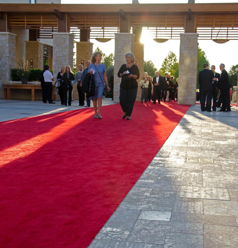 Guests walk along a red carpet outside Sonoma State University's Green Music Center during an evening event, gathering beneath a covered entrance as the setting sun casts long shadows across the plaza.