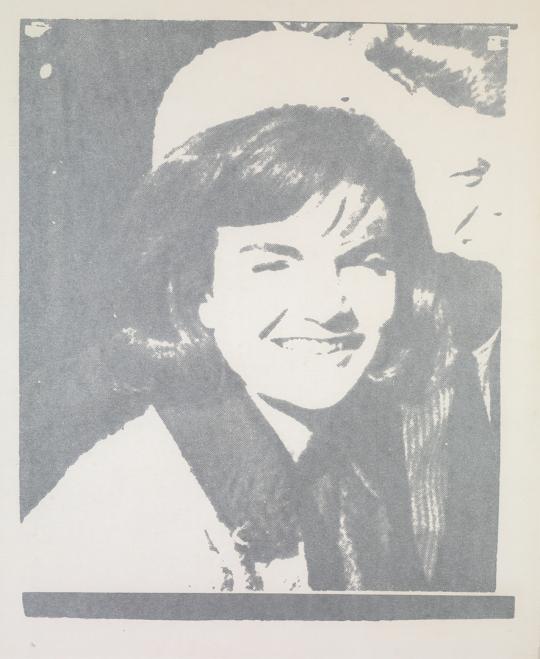 Silkscreen portrait in gray tones showing a smiling woman wearing a hat and coat, rendered in a simplified, high-contrast style. The image has a flat, graphic quality typical of Andy Warhol’s pop art portraits, emphasizing celebrity imagery and mass reproduction